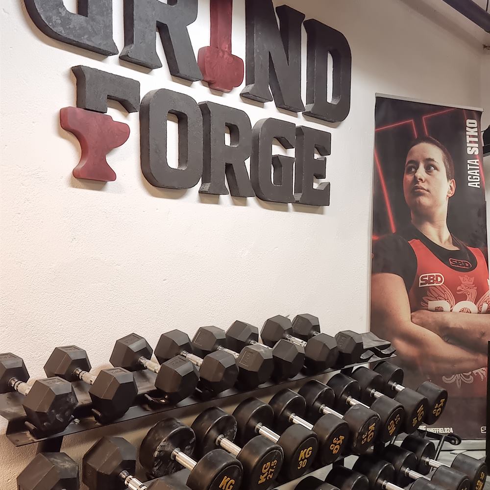 The GrindForge sign on the gym wall, with the Agata Sitko poster and dumbbell racks